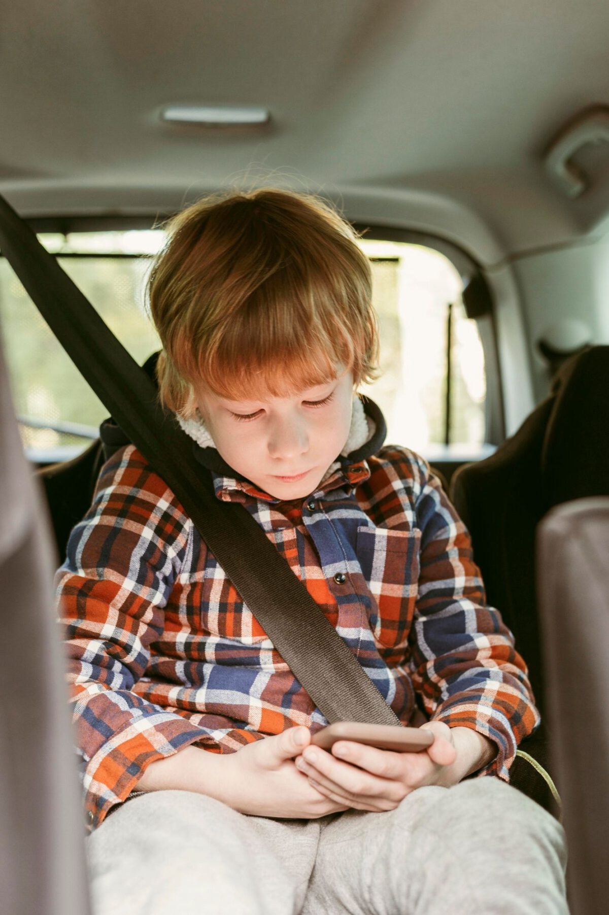 Kind in autobusje, in de gordel en speelt met mobiele telefoon.